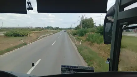 Still in Bosnia, before the border: two lanes on the flat, industrial halls, and the operator’s route card in the glass — Beograd, autoput, g.p. Rača, Bijeljina