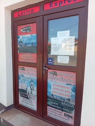 Latino Expres office door on Strada Vlad Țepeș 2, Craiova, with posters for daily coaches and parcels to England and the parcel hours, 16 August 2026