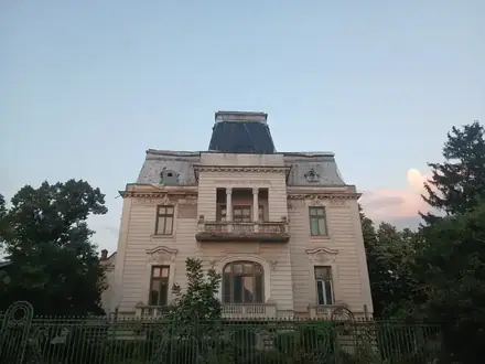 Casa Puiu Pleșia in Craiova — a turn-of-the-century villa with a slate mansard roof, columned loggia and stucco garlands, behind iron railings