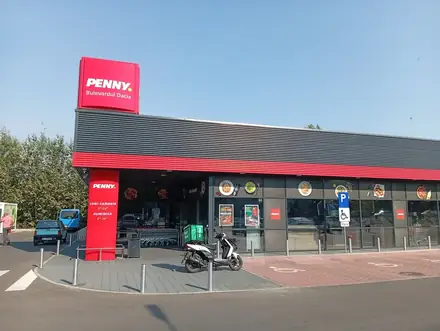 Penny: red pillar with the hours on it, trolleys under the canopy, a courier’s scooter at the door