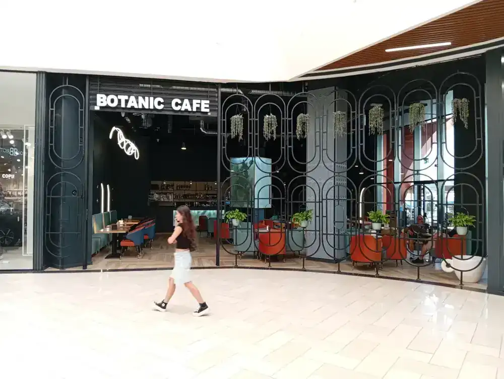 Botanic Cafe on the ground floor — arched screen, hanging plants, velvet seating behind