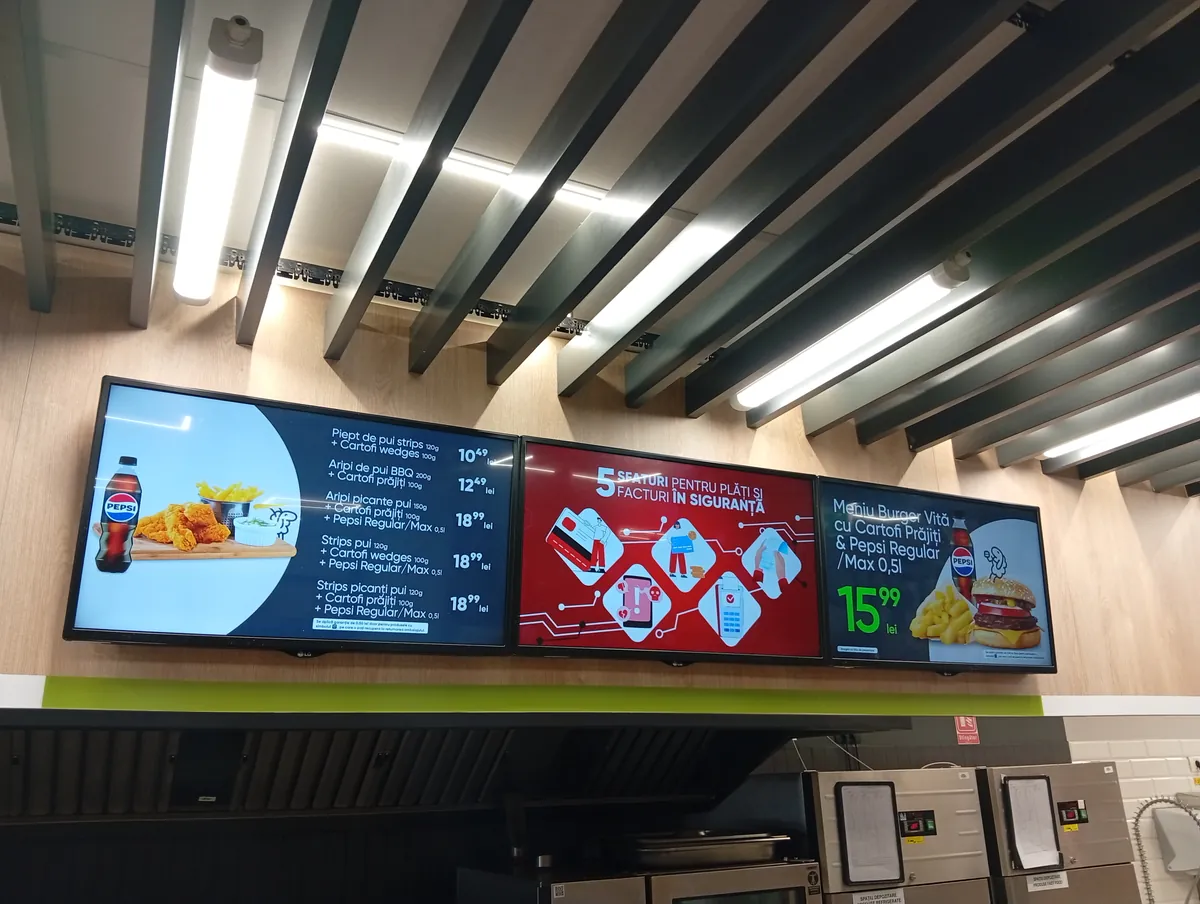 Hot-counter menu screens at Profi Super, Strada Henry Ford, Craiova area: chicken strips, chicken wings and beef burger meals with fries and Pepsi, prices in lei, 22 September 2026