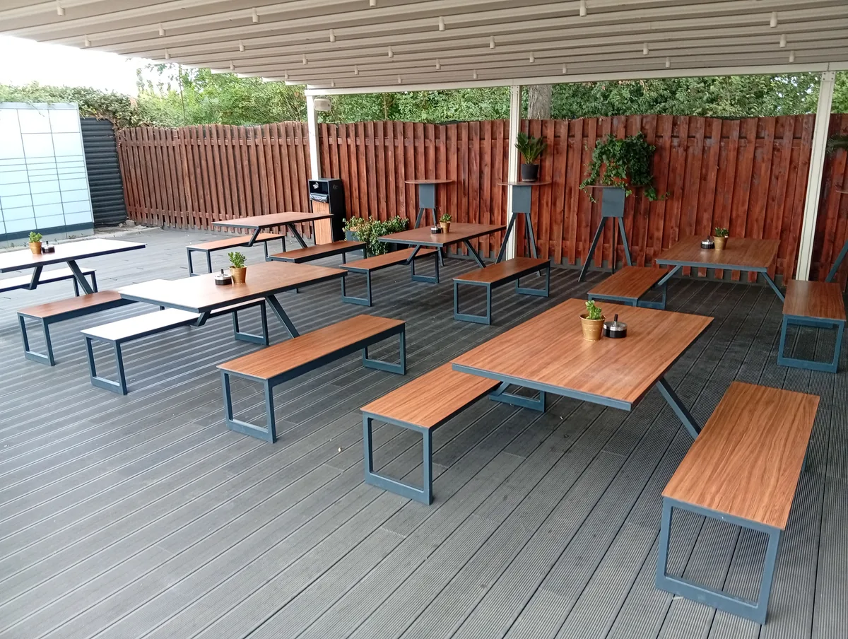 Covered terrace at Drive Grill, Craiova: wooden tables and benches on dark decking behind a red board fence, empty in the afternoon, 22 September 2026