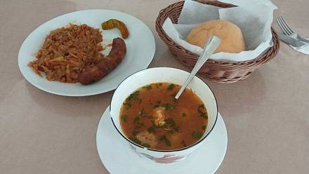 Ciorbă with fresh parsley, sausage with stewed cabbage and a basket of bread at Landhaus Restaurant, Craiova