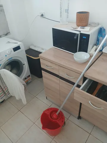 The kitchen the next morning, washer door open, a red mop bucket on the floor
