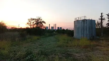 The towers and chimneys at sunset from the east side — the downwind side — an old tank in the foreground. Taken from the point on the map below, 10.9 km away; in late summer the sun goes down straight behind the stacks from here